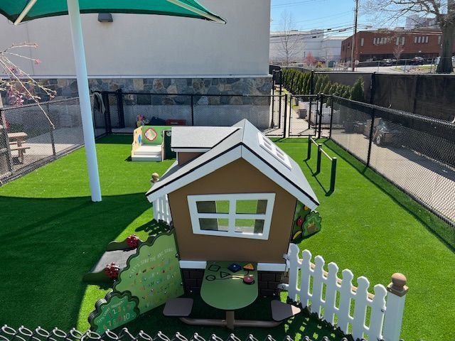Playhouse on artificial turf in a fenced yard; green canopy overhead.