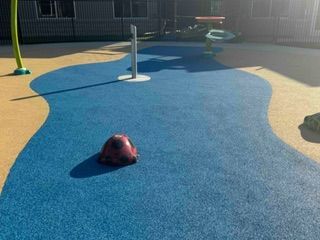 Playground with blue and yellow safety surfacing, a rock, and water features.