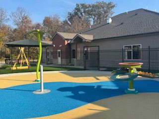 Playground with water features in front of a building with a fenced area.