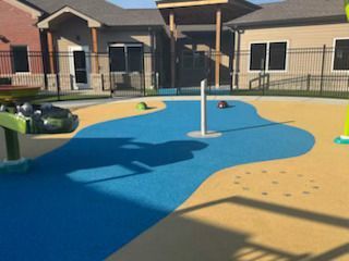 Playground with blue and tan surfacing, water features, and a building in the background.