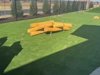 Logs arranged on green artificial turf in a fenced area.