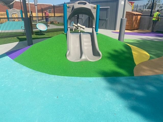 Playground with a slide on a green mound, blue, purple, and yellow ground.