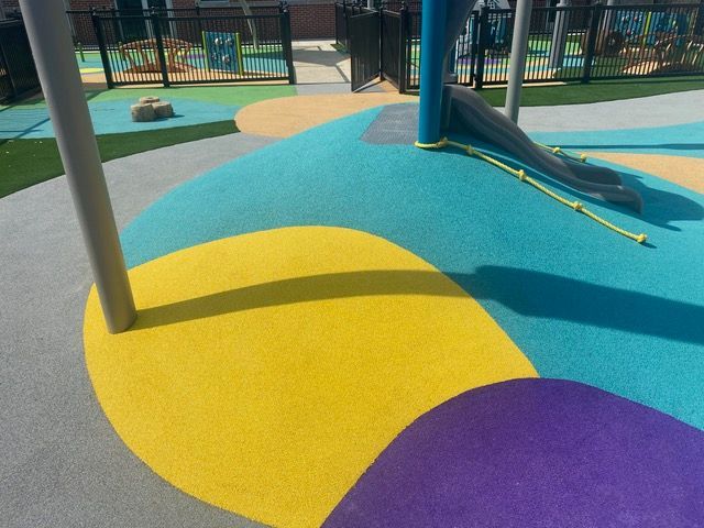 Colorful playground surface with yellow, teal, purple, gray, and green areas.