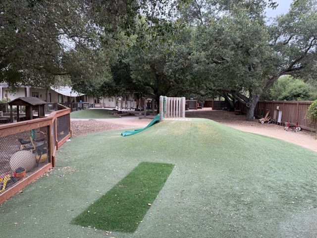Playground with artificial turf, small hill with a slide, and a wooden fence.