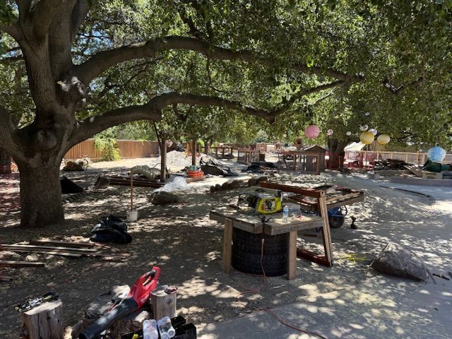 Outdoor area with construction materials under large trees, possibly a party setup.