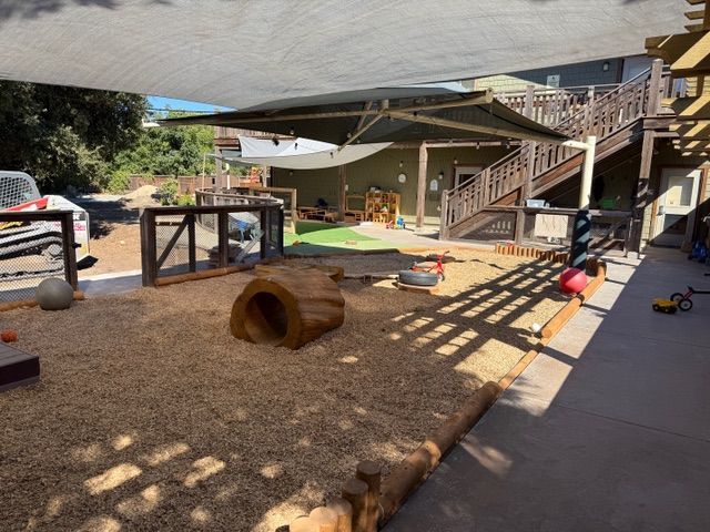Playground with wood chips, shade structure, wooden structures, and play equipment.