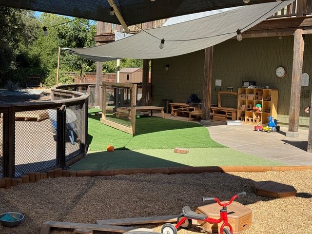 Playground with shade cover, sand area, grass, and toys.