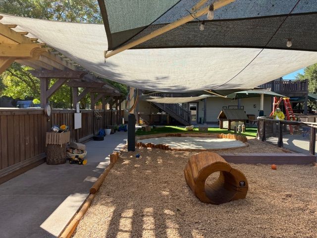 Playground with shade sails, wood chips, and wooden structures.