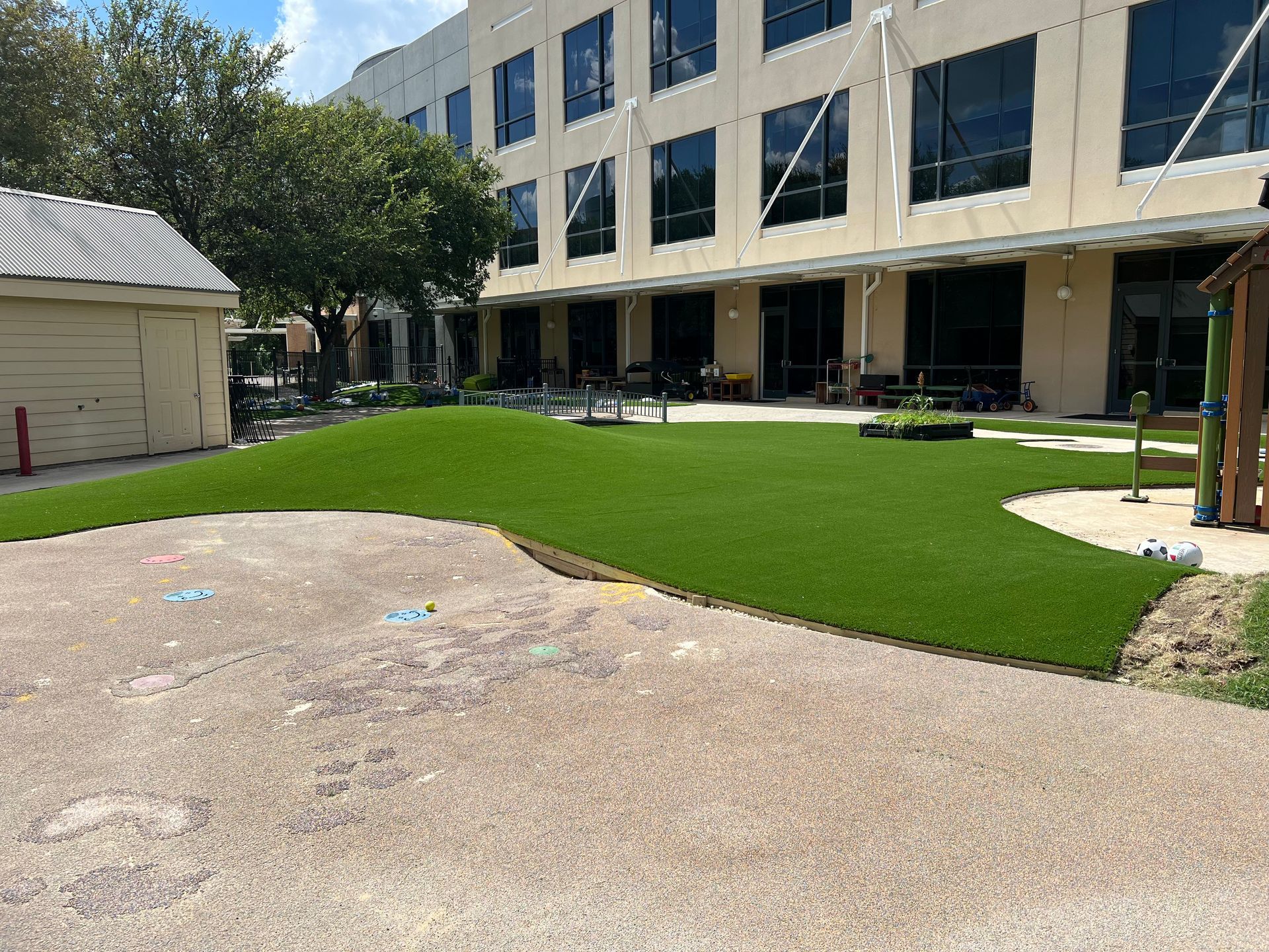 Artificial turf in courtyard next to a building. Concrete area in foreground.