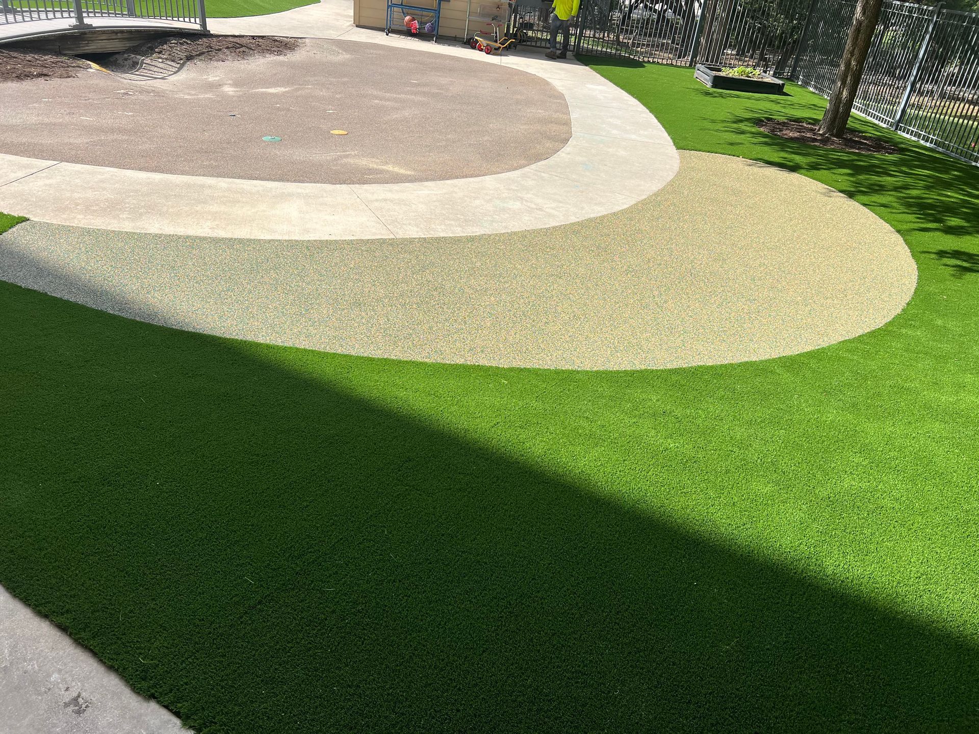 Bright green artificial turf with a light tan gravel play area and concrete path.
