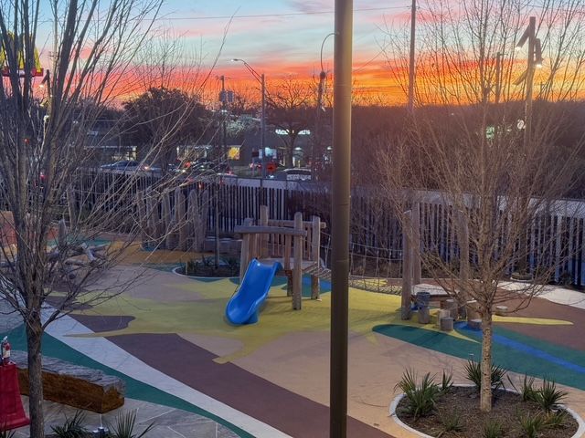 A colorful playground with a blue slide under a vibrant sunset sky.