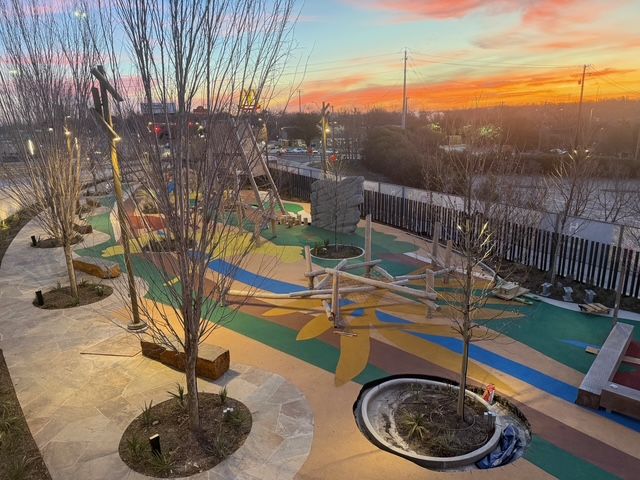 A colorful playground with trees, benches, and climbing structures during a vibrant orange and pink sunset.