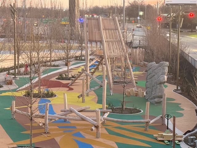 A vibrant playground with wooden climbing structures, a rock wall, and a colorful, patterned ground surface.
