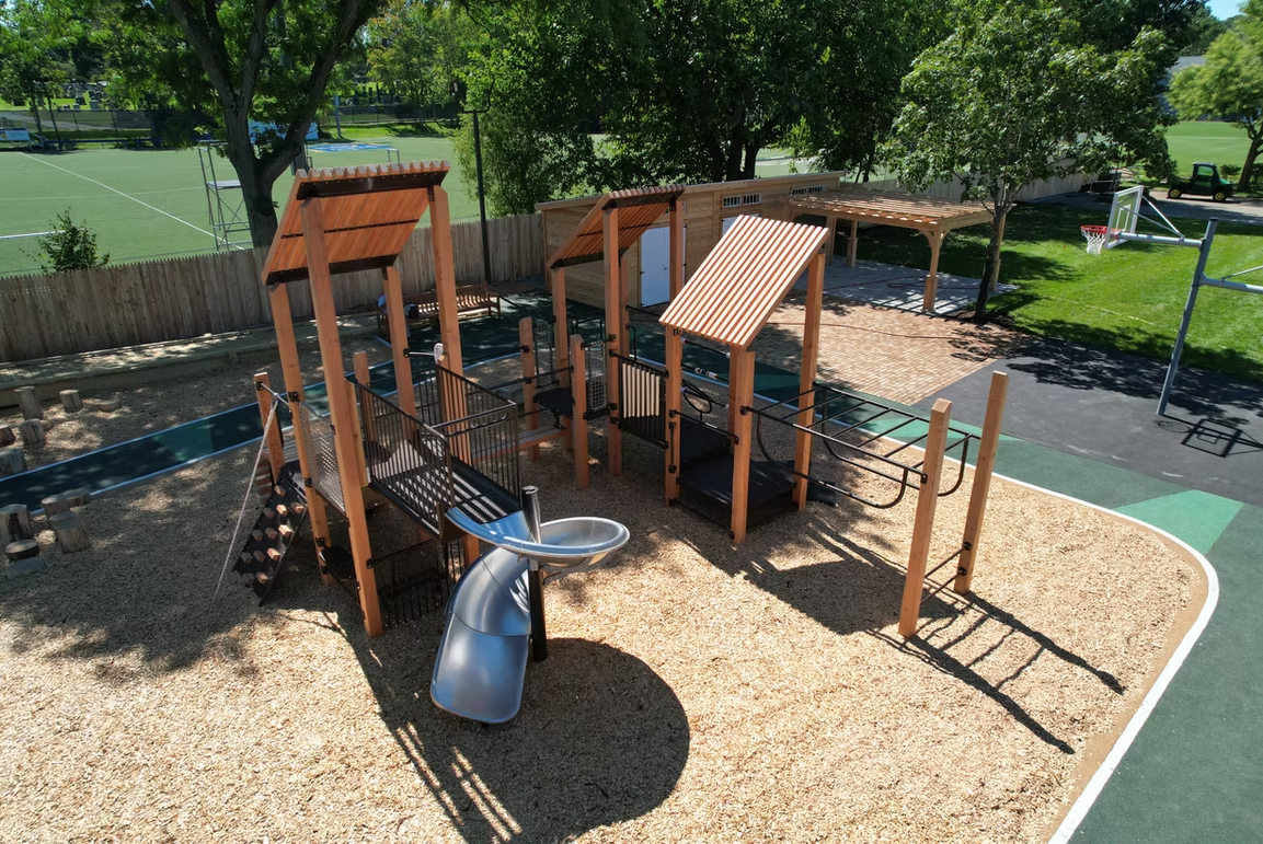 Playground with wooden structures, slides, and climbing features on wood chip ground.
