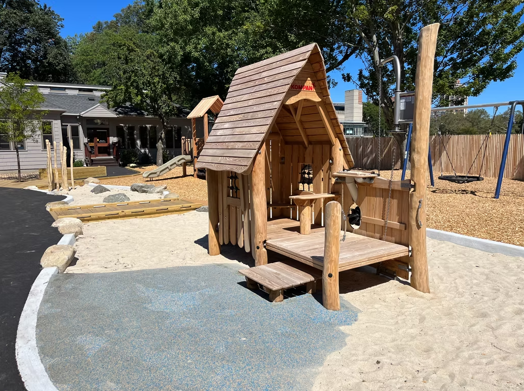 Playhouse structure on a playground with wood beams, gravel, and a basketball hoop.