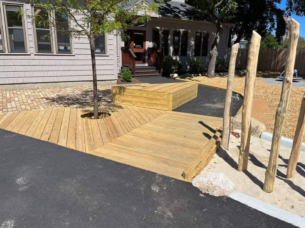 Wooden deck and path leading to a house entrance. Includes steps, tree, and decorative log posts.