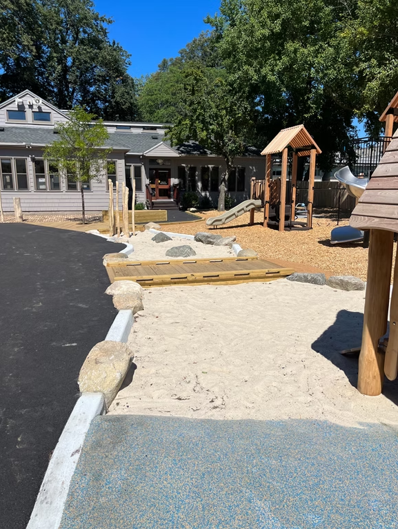 Playground with sand pit, climbing structure, and building in the background.