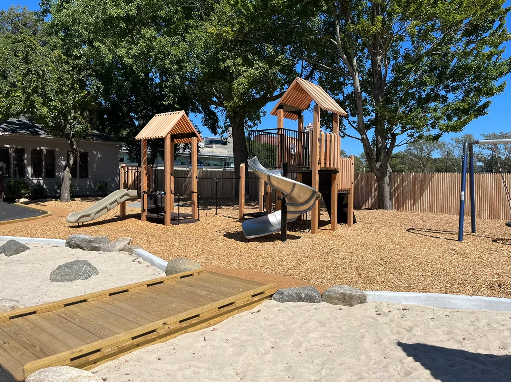 Playground with wood structures, slides, bridge, and wood chips, under blue sky.