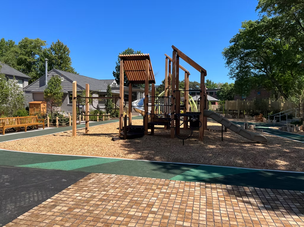 Playground with wooden structures, slide, and wood chip ground cover; blue sky backdrop.