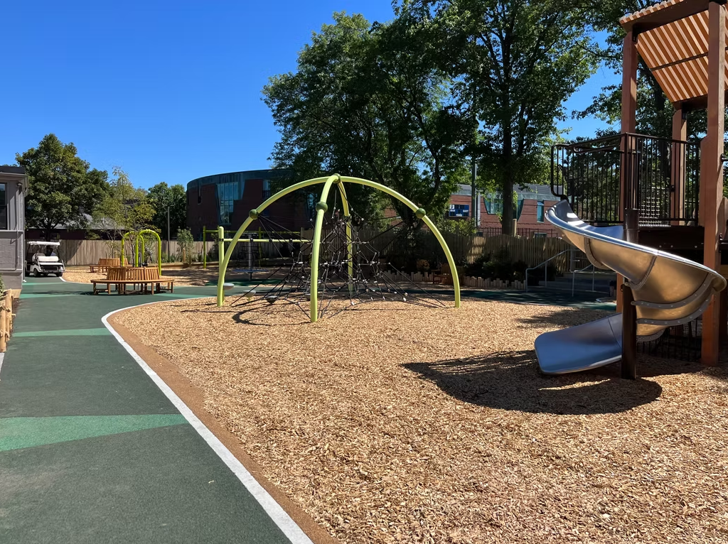 Playground with wood chip ground cover, climbing structure, slide, and picnic tables.