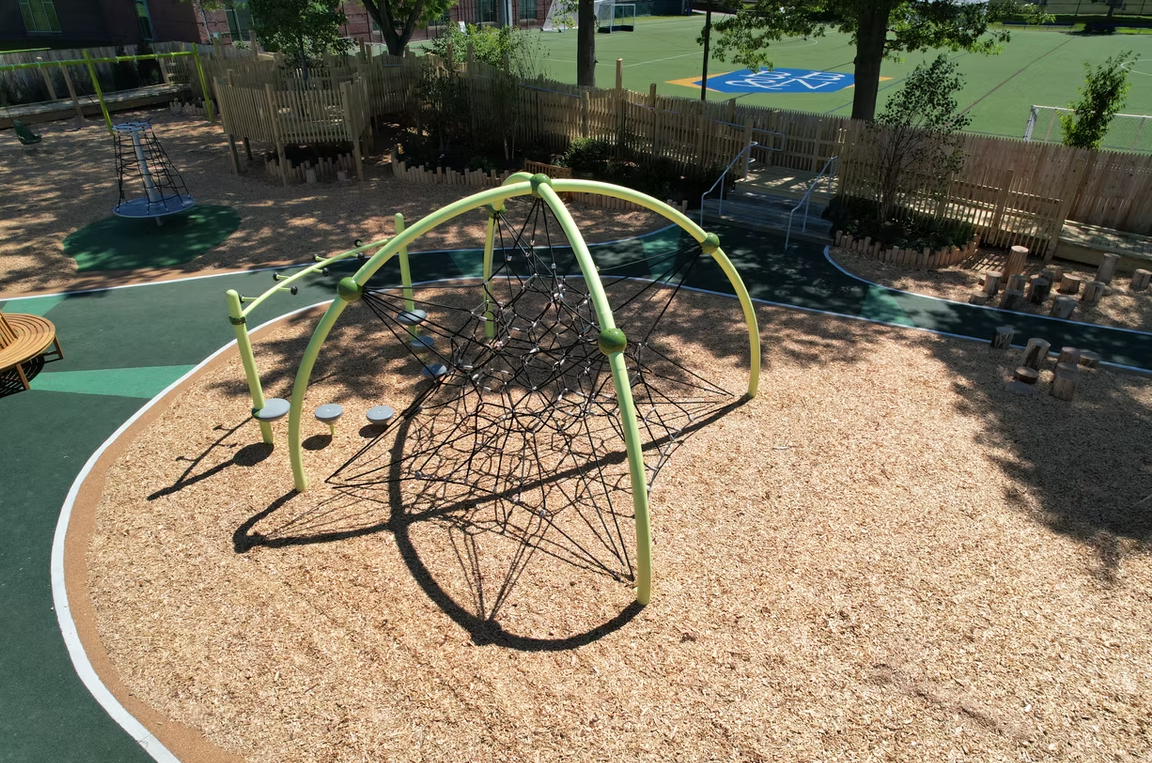 Playground with green climbing dome, wood chips, and bordering fence.