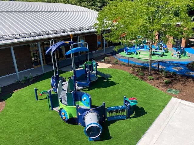 Playground with blue and green equipment, green turf, and building in the background.