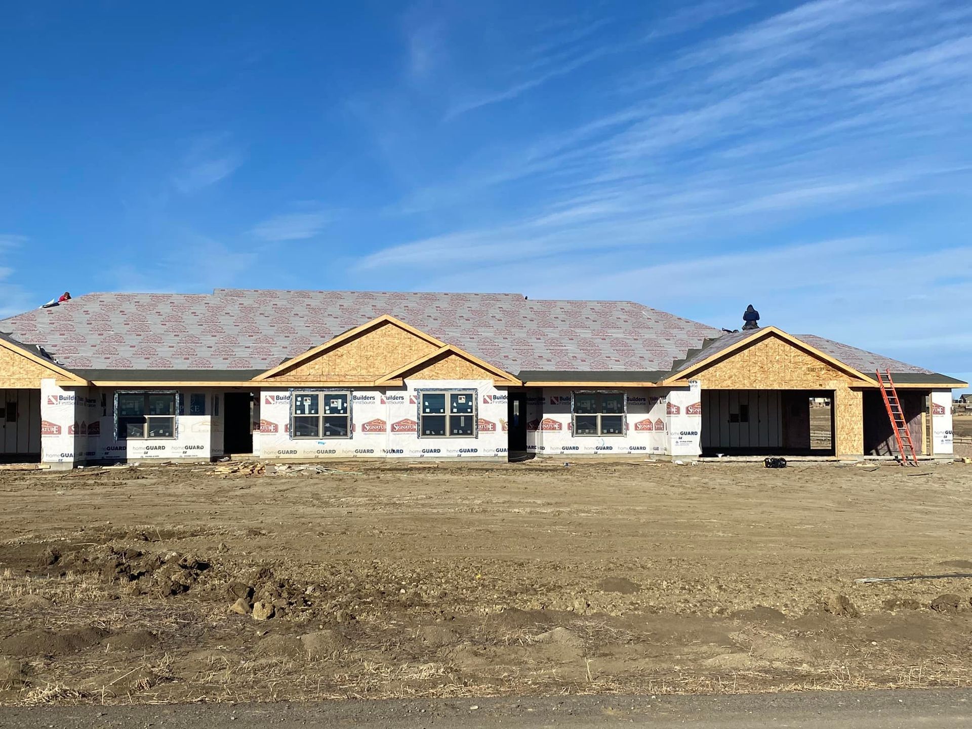 Multi-unit homes under construction on a field, blue sky.