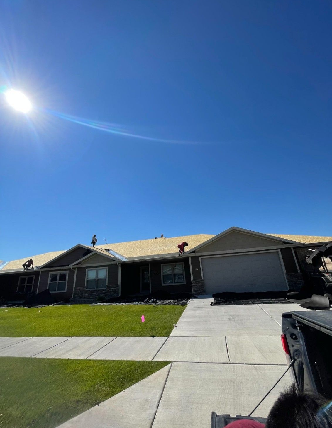 House with partial new roof. Clear blue sky, sunny day. Driveway, green lawn.