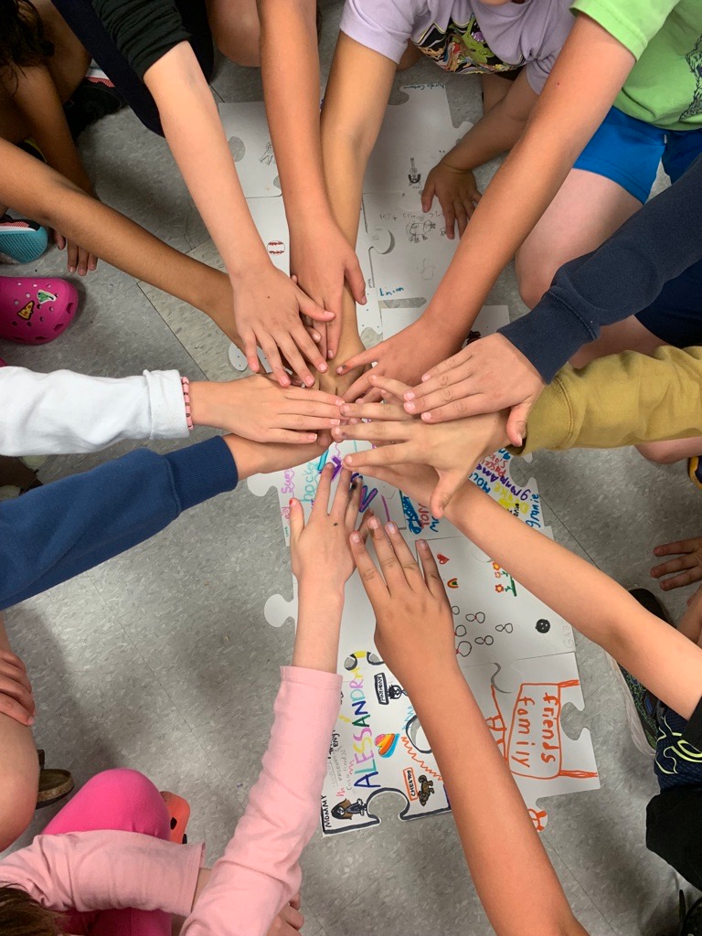 A group of children are putting their hands together in a circle.