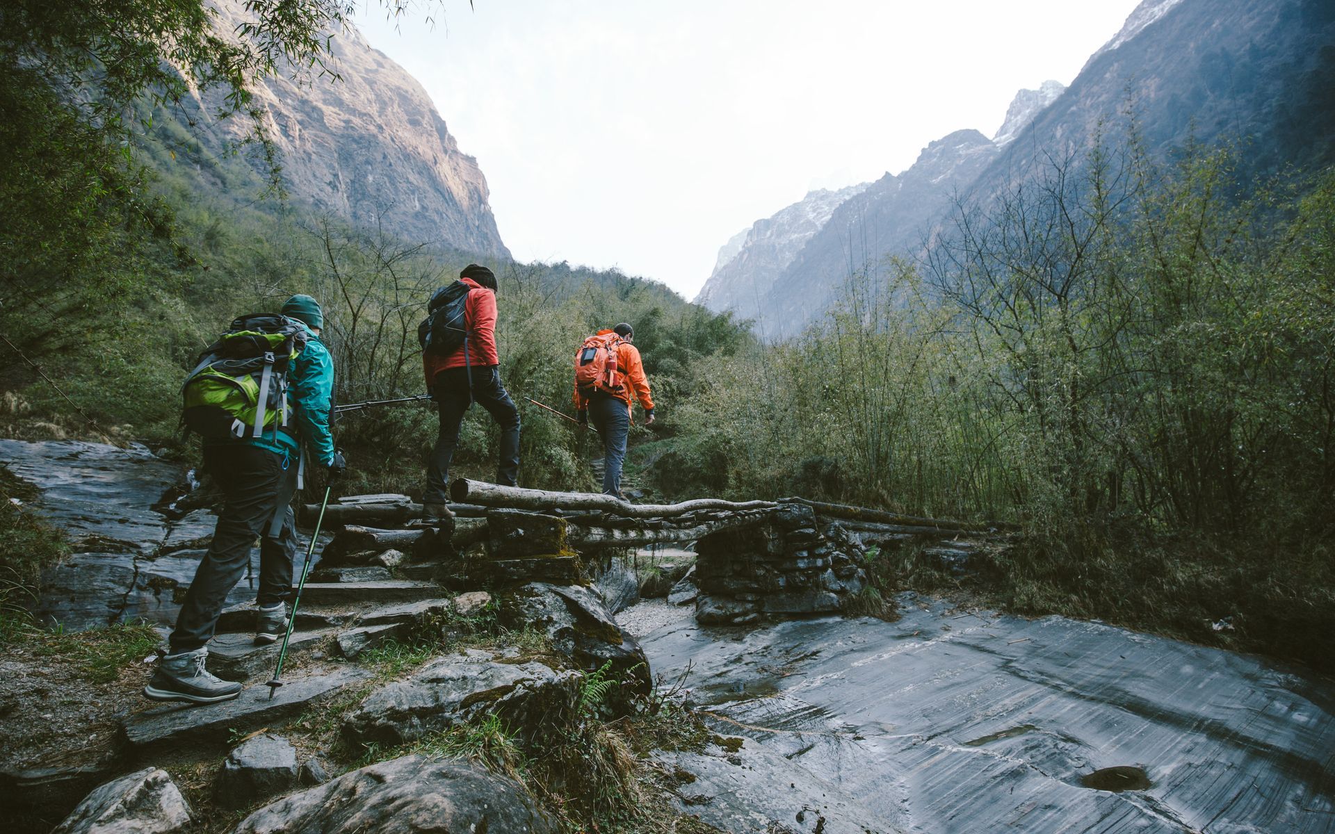 Hikers walking on stone steps through a mountain valley; three people with backpacks.