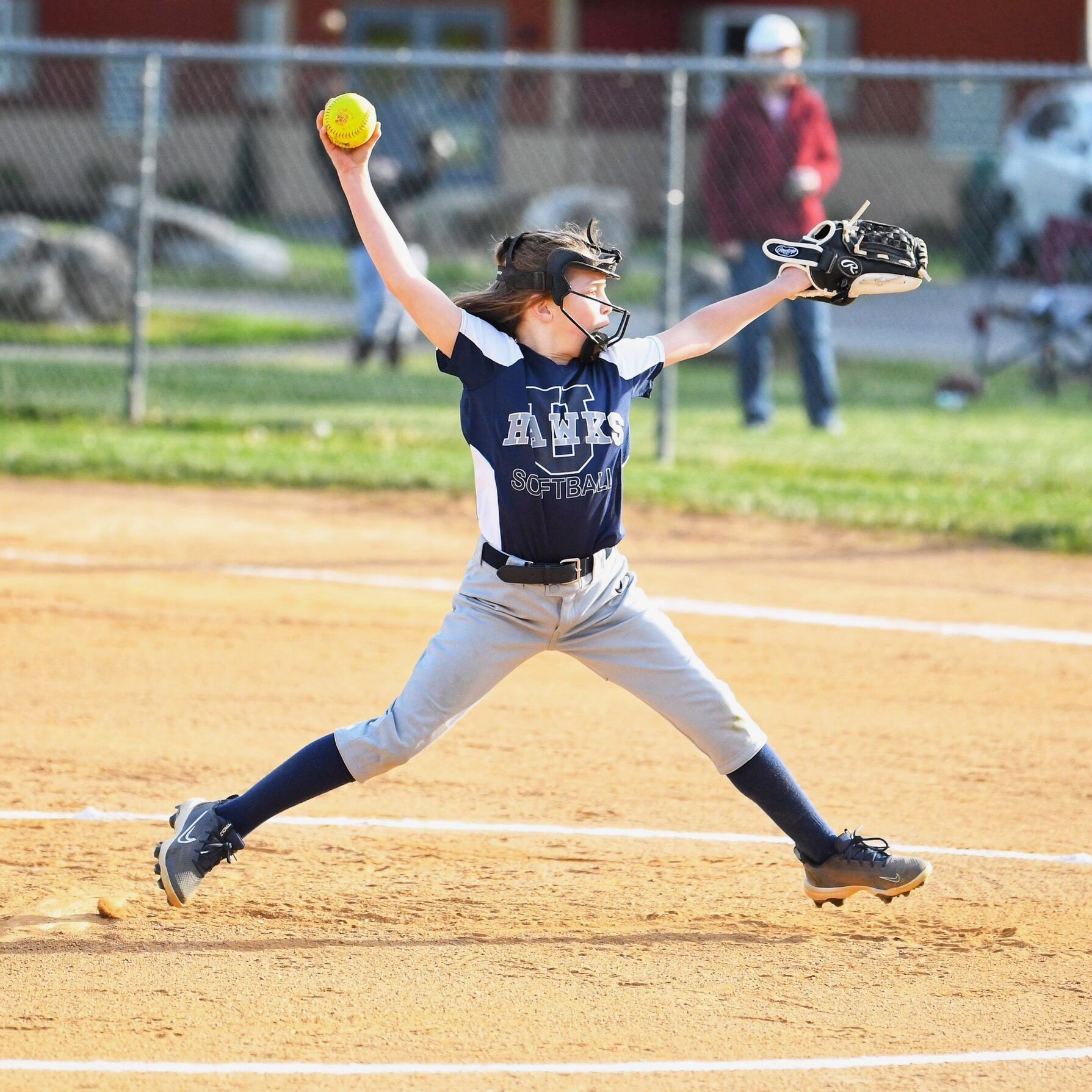 Softball players on a field. One swings a bat as another prepares to catch the ball. Others in the background.