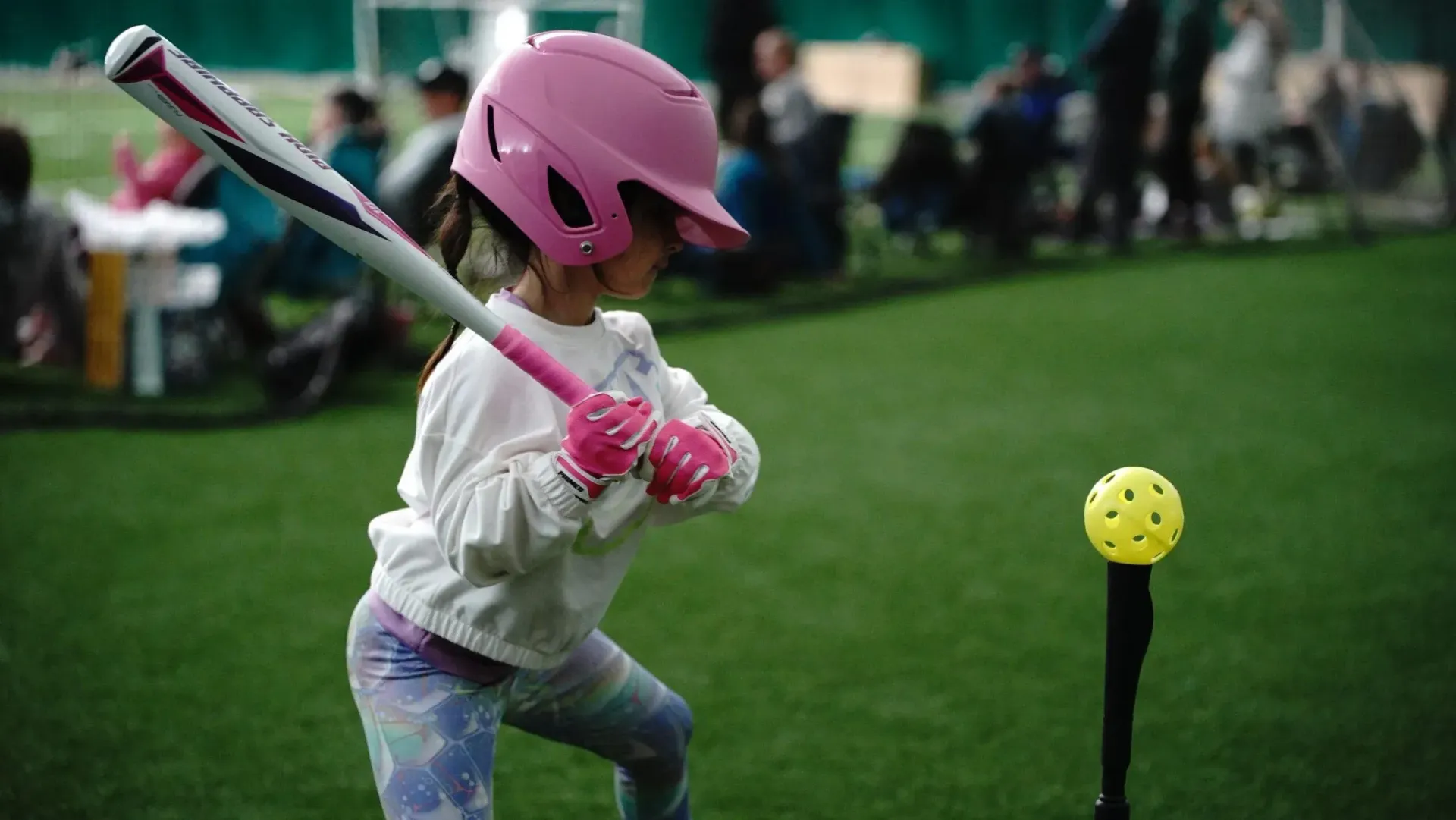 Softball player swinging bat at a yellow ball, wearing helmet, knee pads, and uniform in a dirt field.