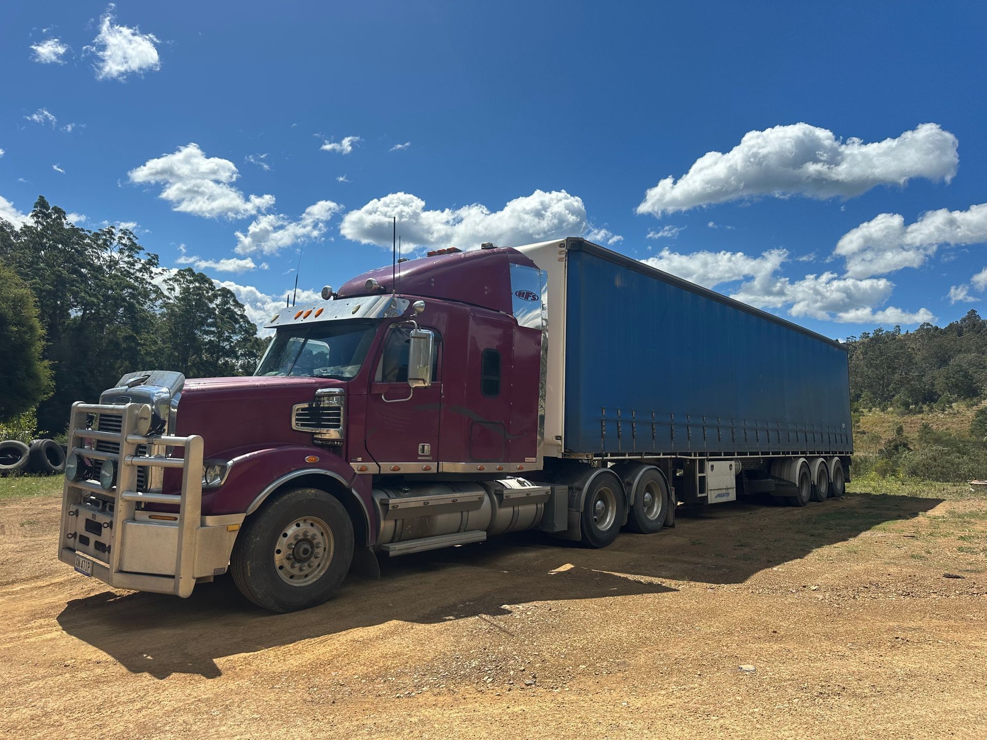 Maroon semi-truck with a blue trailer parked on dirt — D & M Freighters Water In Bucca Wauka, NSW