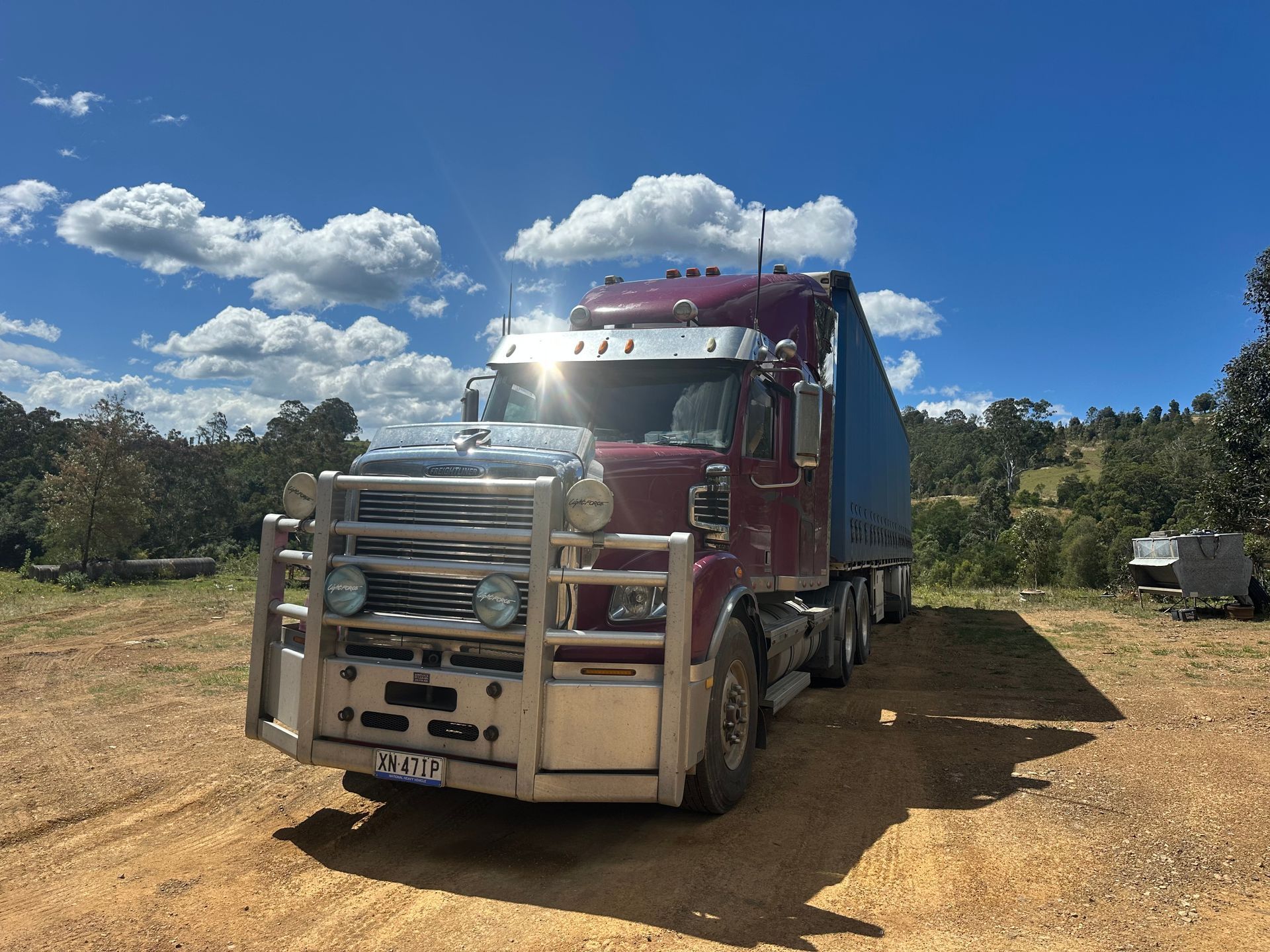 Red semi-truck with bull bar on a dirt road under a bright blue sky with clouds — D & M Freighters Water In Bulahdelah, NSW