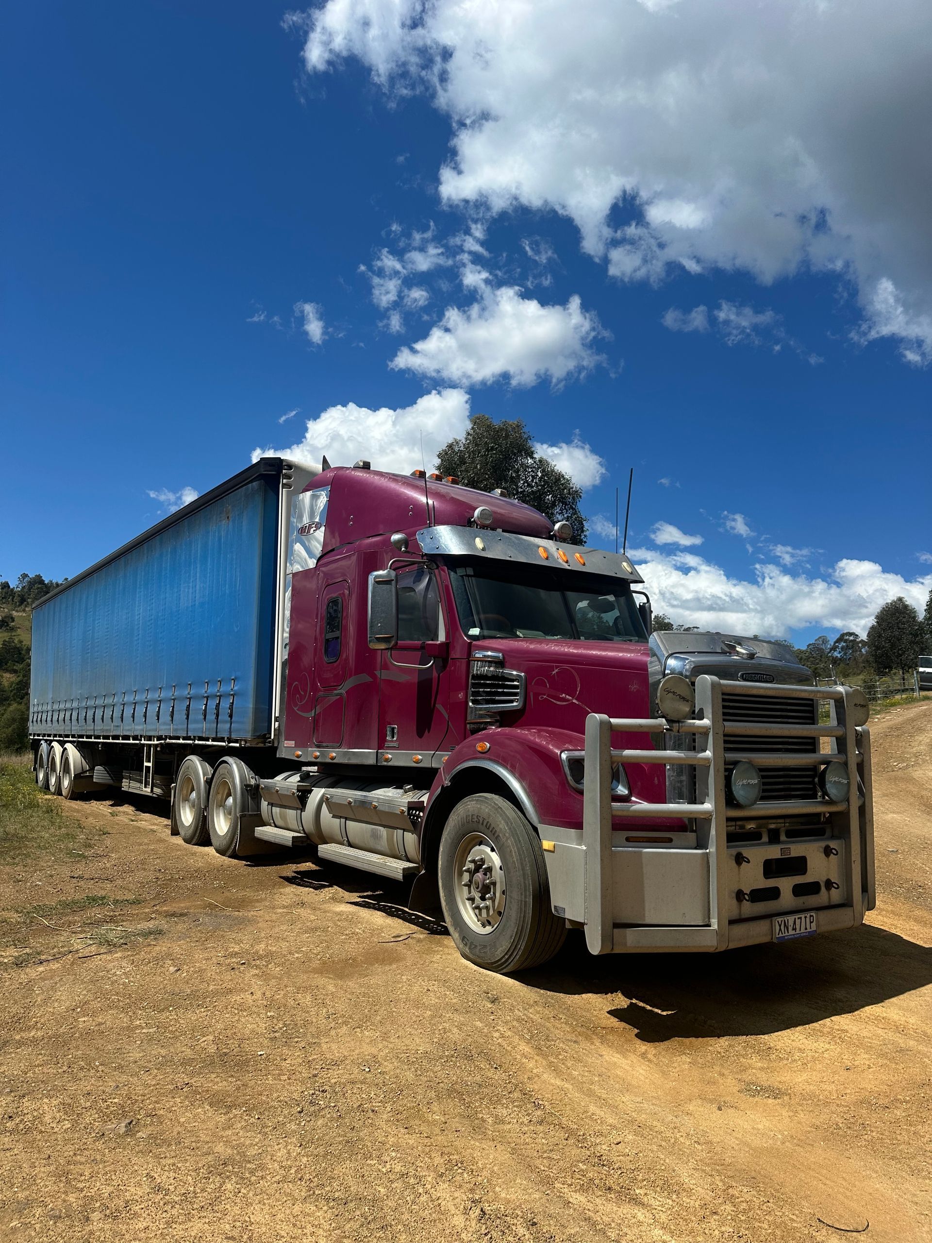 A maroon freighter truck with a blue trailer parked on a dirt road under a partly cloudy blue sky — D & M Freighters Water In Nabiac, NSW