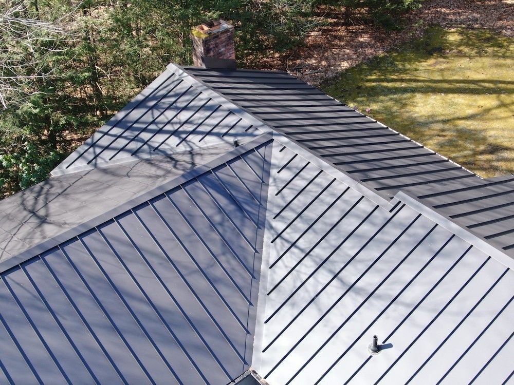 Roof with gray metal panels and a chimney, viewed from above near trees.