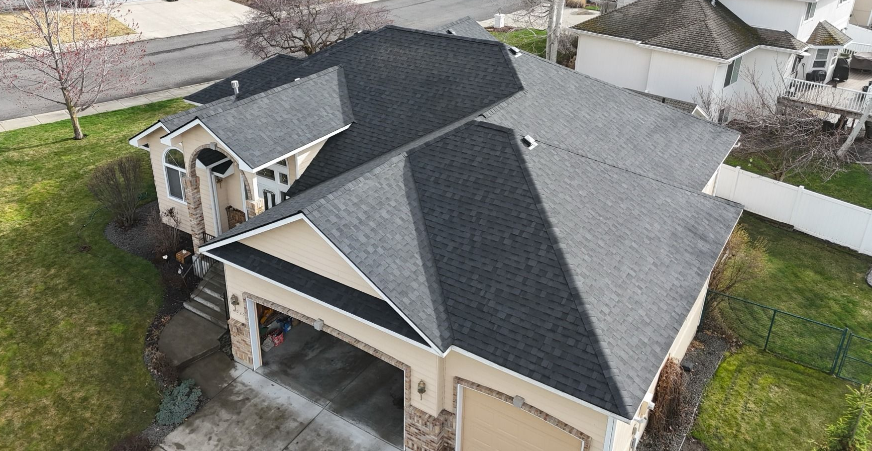 Aerial view of a beige suburban house with a dark gray roof, garage, and front porch.