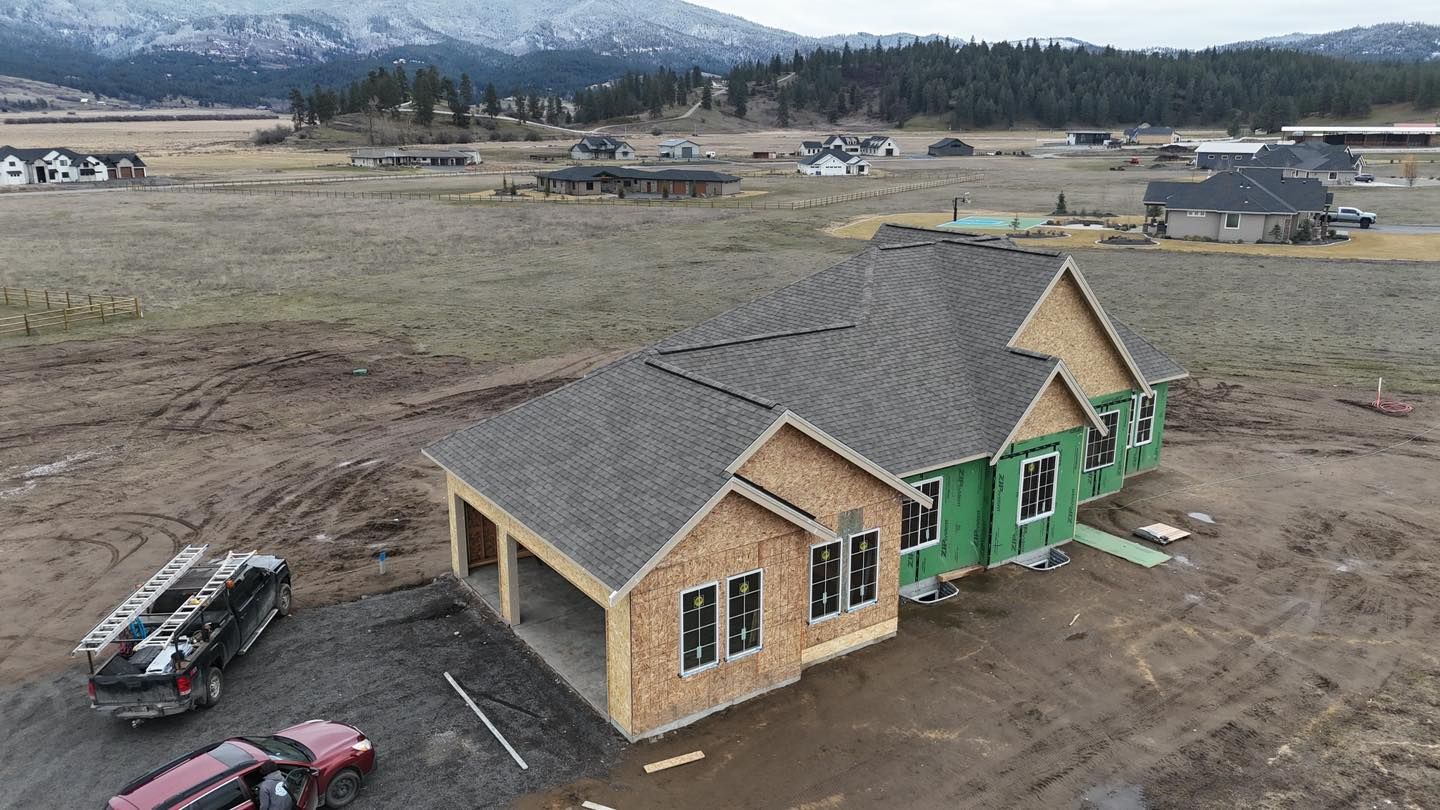 Partially finished house with gray roof and green siding in a rural construction site with mountains beyond