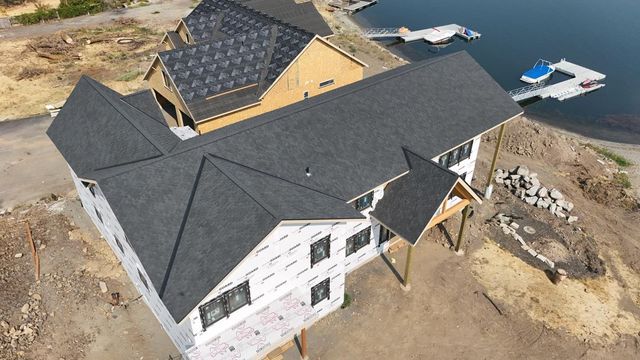 Aerial view of a house under construction with dark roof shingles near a body of water.