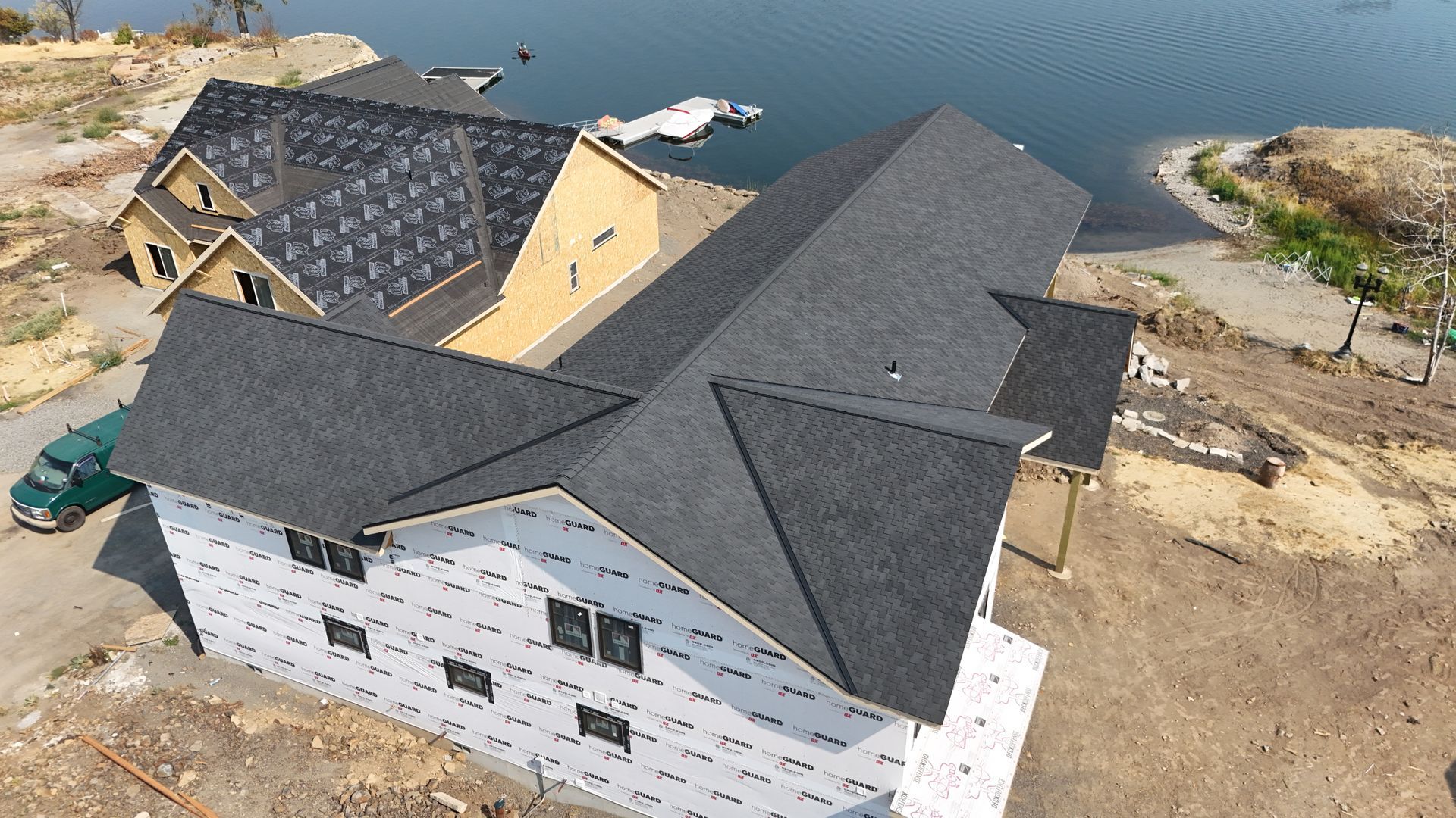 Aerial view of a large house with dark gray roof panels near the water’s edge.