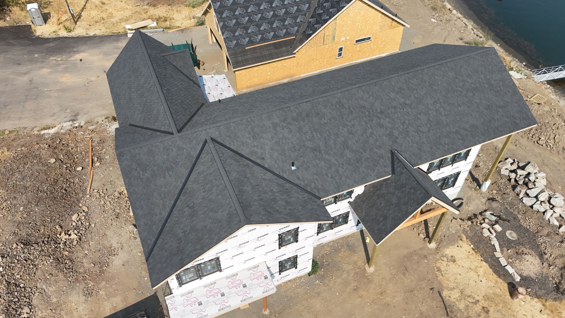 Aerial view of a large house with dark gray roof under construction on a dirt lot