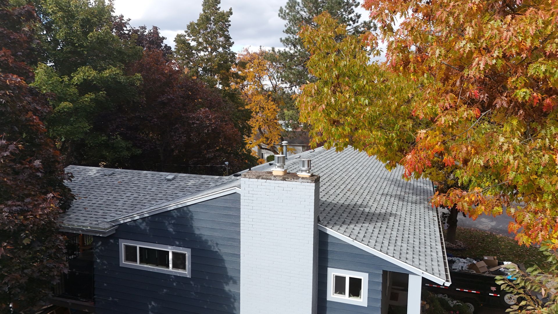 House with gray roof and chimney surrounded by autumn trees with orange and red leaves