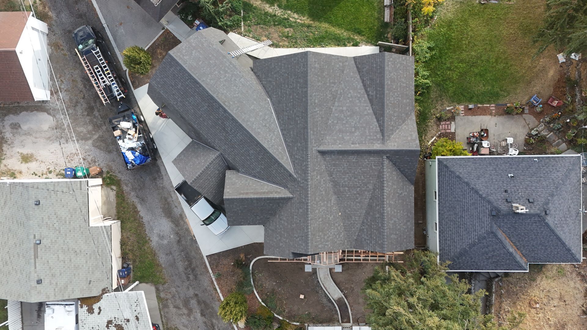 Aerial view of a gray-roofed house with a driveway, neighboring homes, and trees.