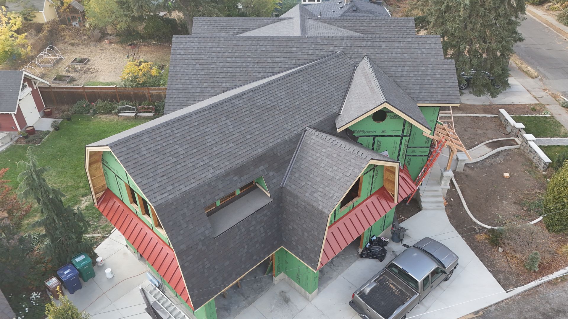 Aerial view of a large house with a dark gray roof, red and green exterior, and parked cars below.