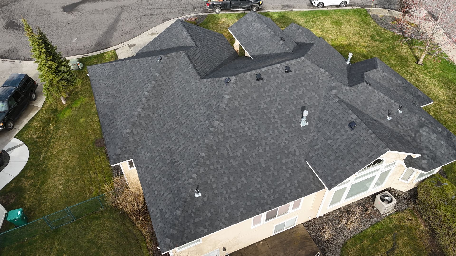 Aerial view of a house with a dark gray roof and light-colored siding, surrounded by grass and a driveway.
