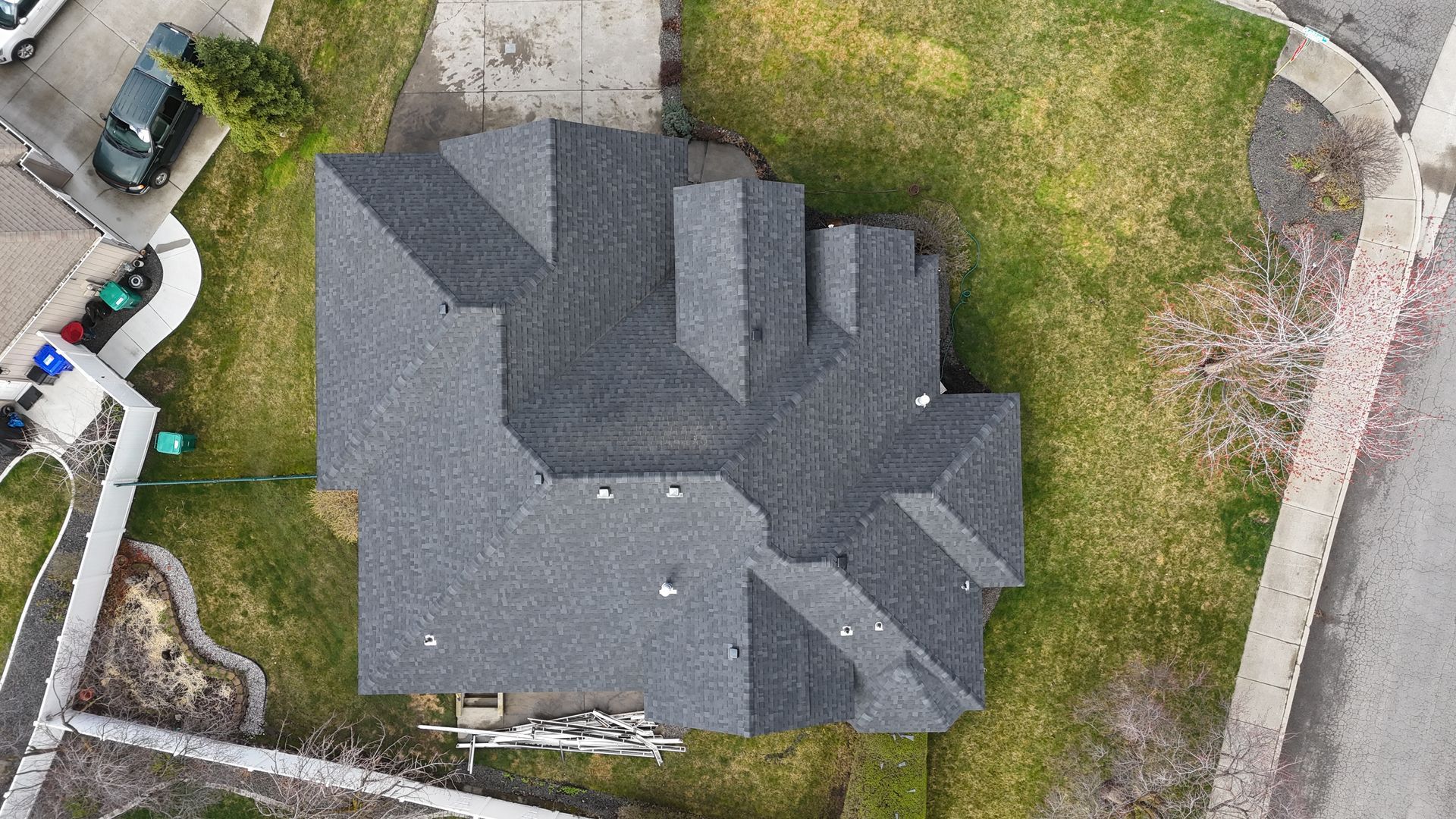 Aerial view of a dark gray house roof surrounded by grass and a driveway.