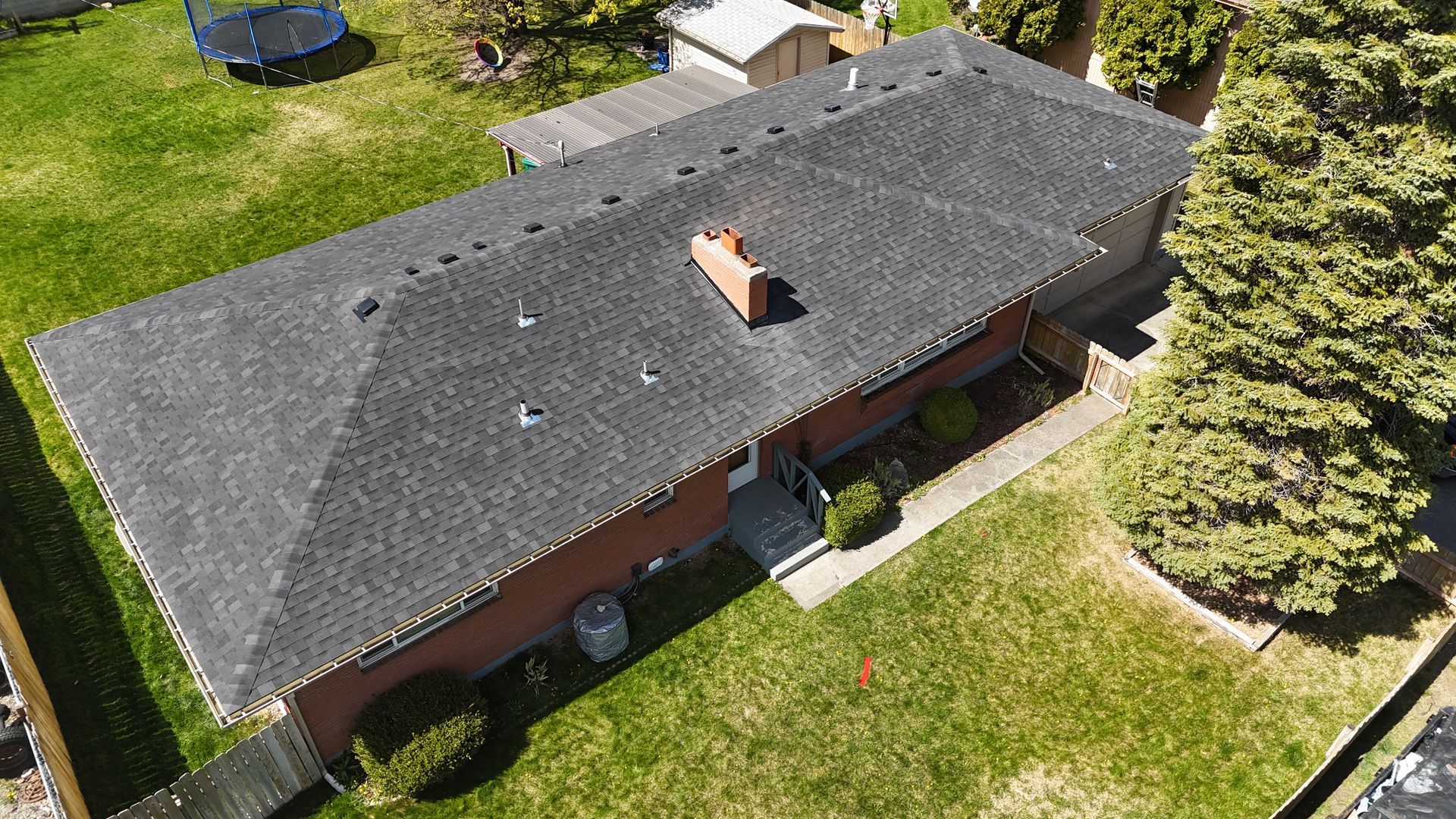 Aerial view of a single-story house with a dark shingled roof and green lawn.