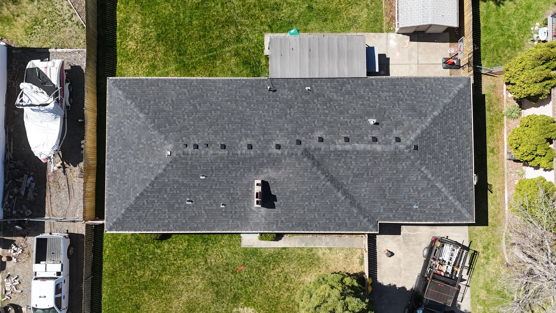 Aerial view of a house with a dark gray roof, green lawn, and parked cars along the driveway and street.