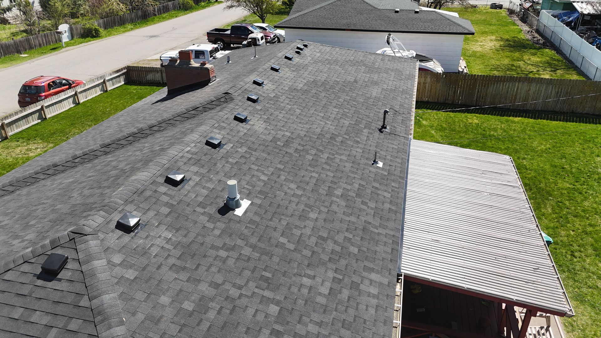 Aerial view of a gray shingled rooftop with several vents beside a driveway and hedges.