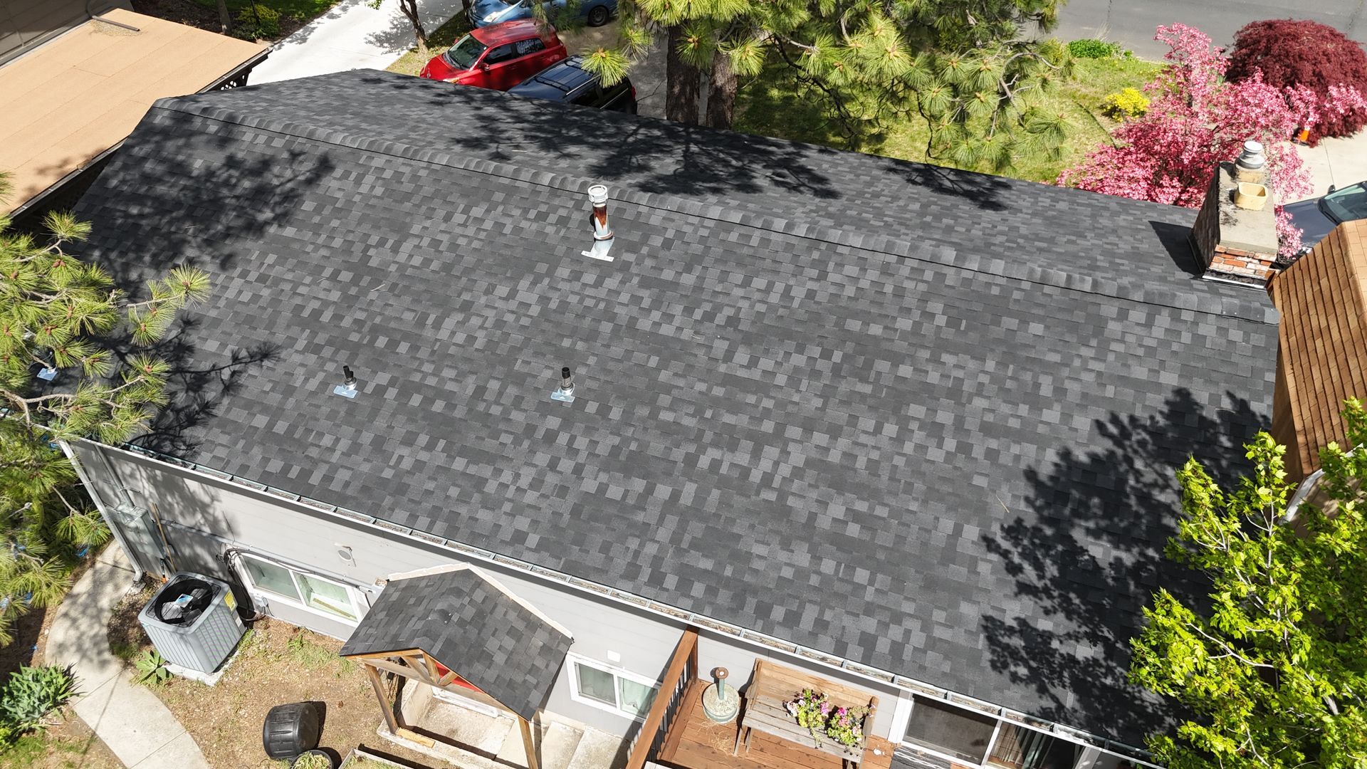 Aerial view of a house with a dark shingled roof, trees around it, and a red vehicle nearby.